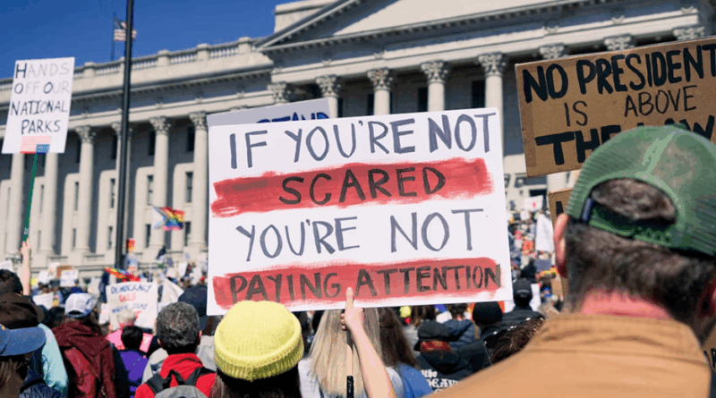 A sign protesting the actions of Donald Trump and Elon Musk being held up at the Hands Off protest outside the Utah State Capitol to represent your finances under fascism